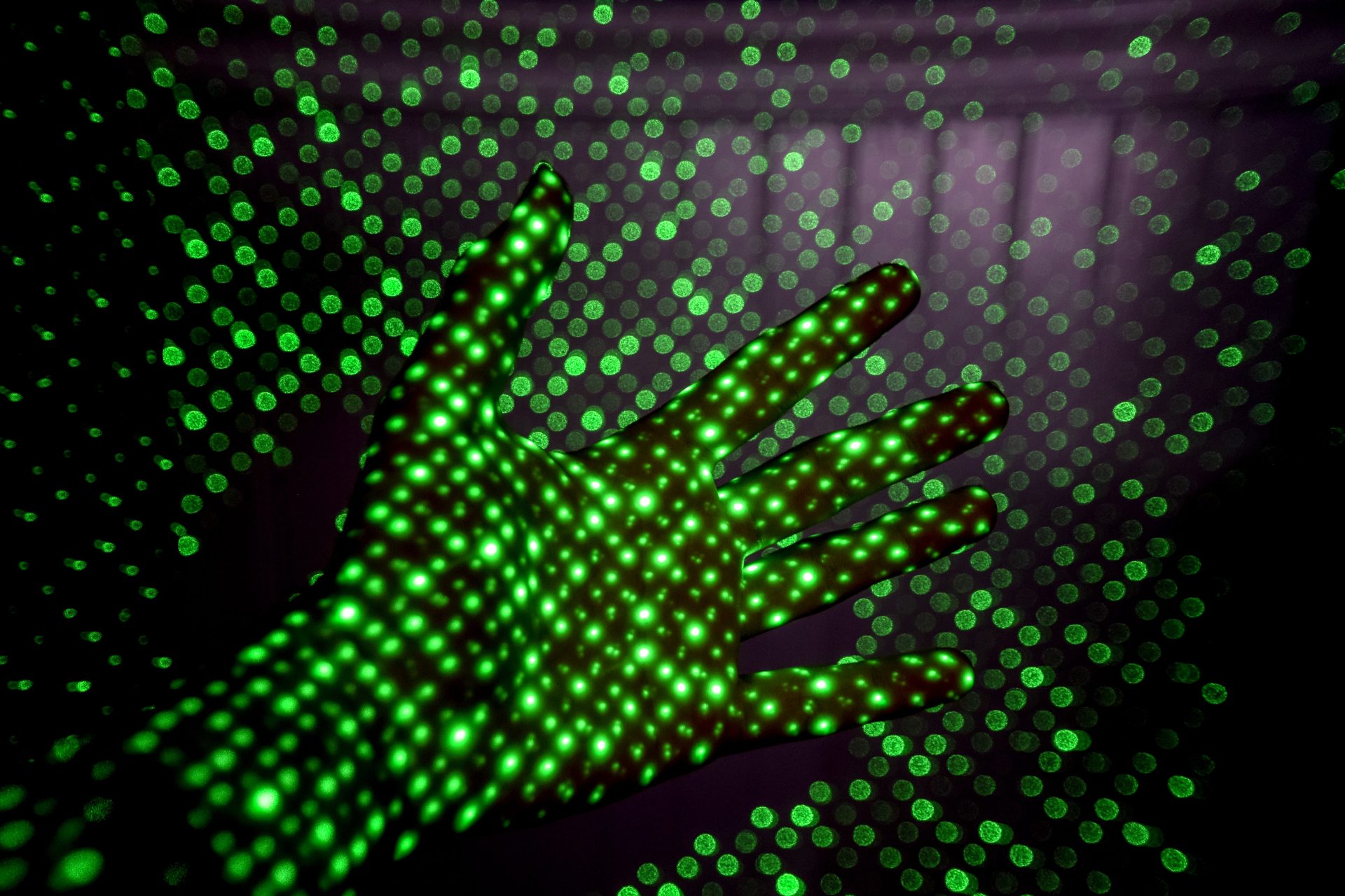 Hand med gröna ljusprickar från laser.