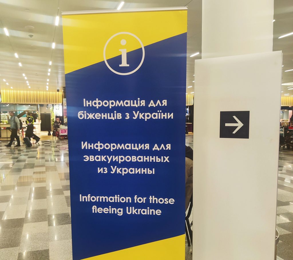Inomhus på flygplats. Roll up i gult och blått med informationstext på ukrainska för de som flyr från Ukraina.