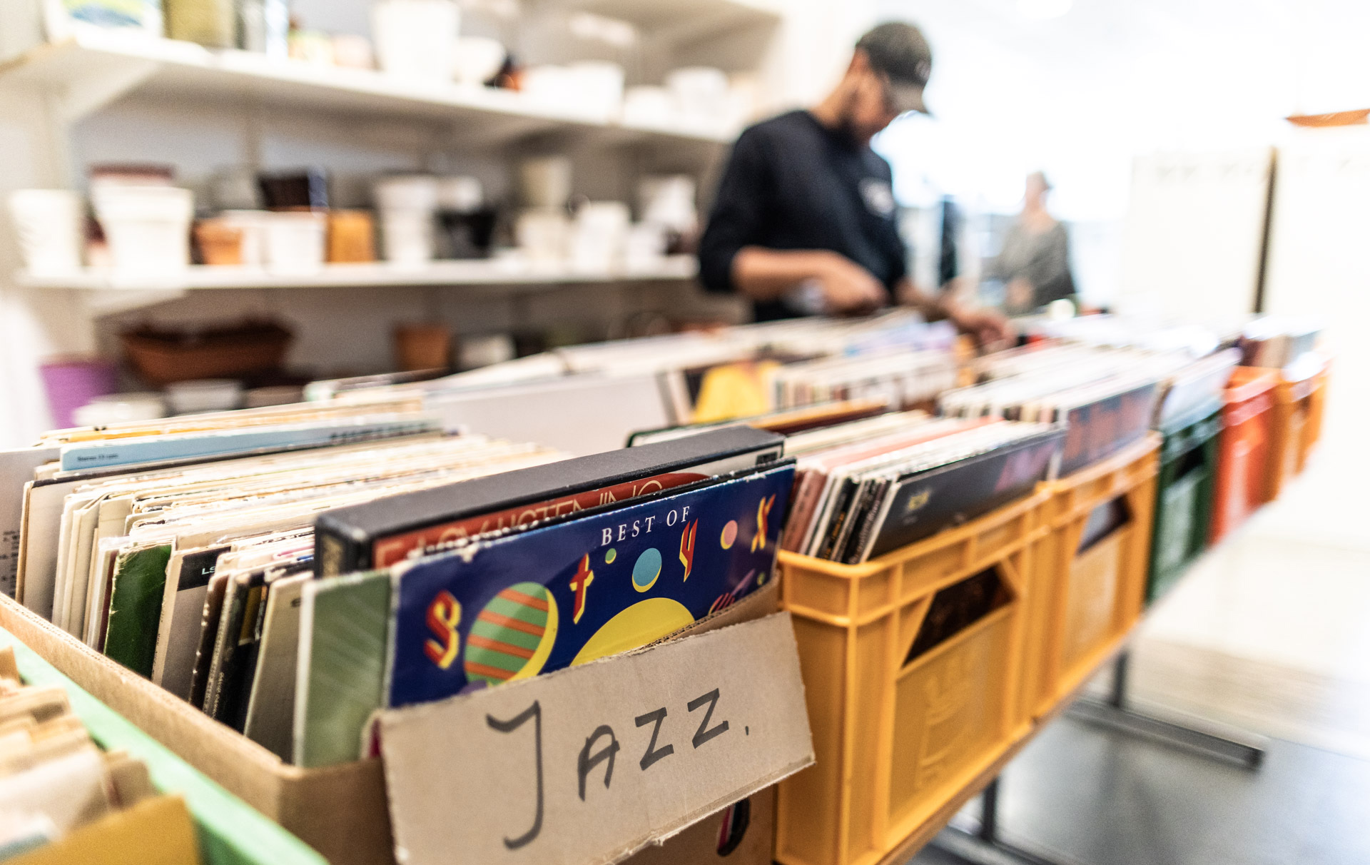 Inomhus i en butik. I förgrunden står plastbackar med LP-skivor med en skylt som det står jazz på. I bakgrunden en person som står och bläddrar bland skivorna.