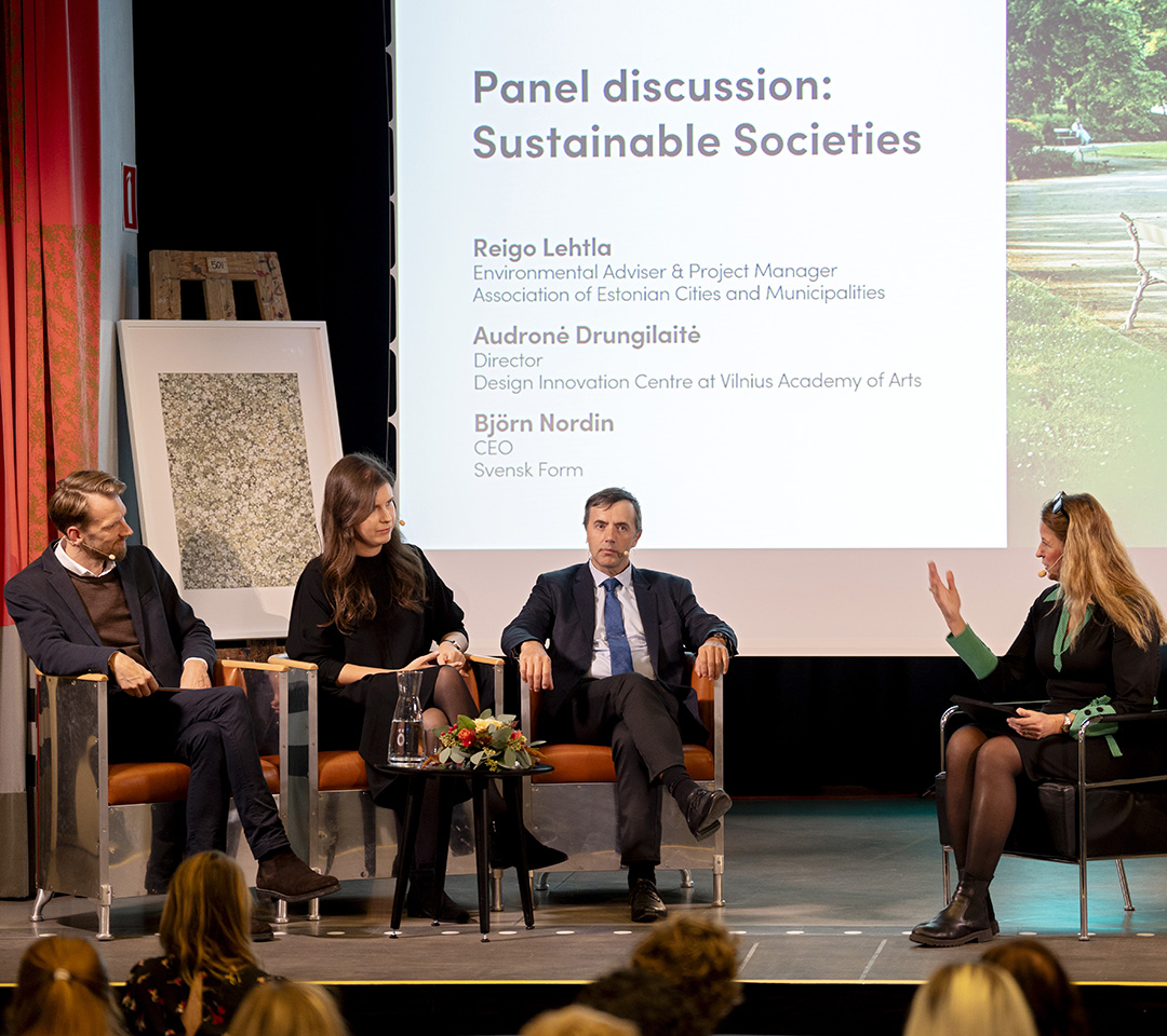 Inomhus i en konferenssal. Fyra personer som sitter på en scen och pratar i ett panelsamtal. I förgrunden sitter personer och lyssnar.