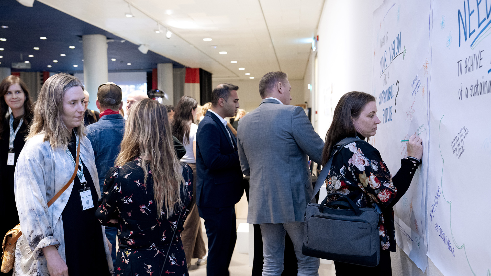 Inomhus i en konferenslokal. Personer som står och skriver på stora plakat på en vägg.